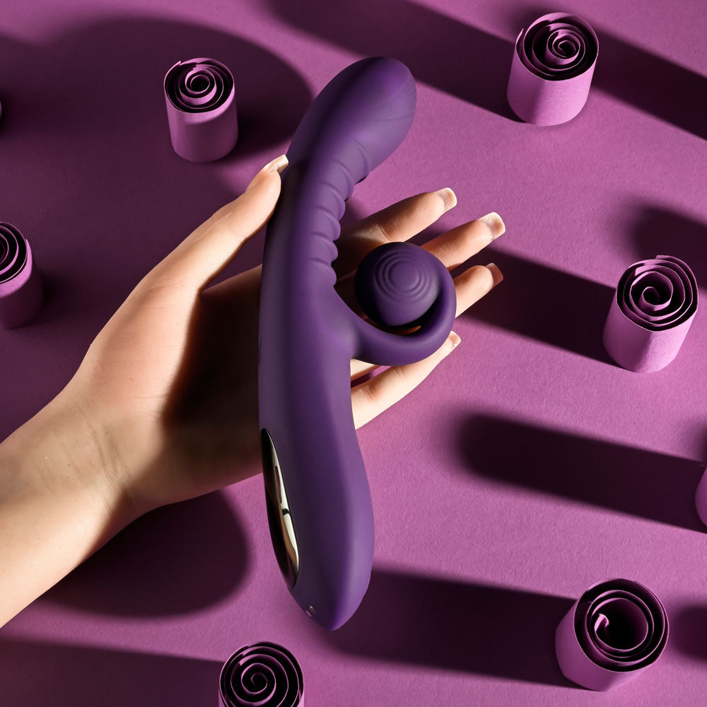 Playboy CURLICUE -  23.5 cm USB Rechargeable Rabbit Vibrator in hand on a vibrant purple background with decorative swirls.
