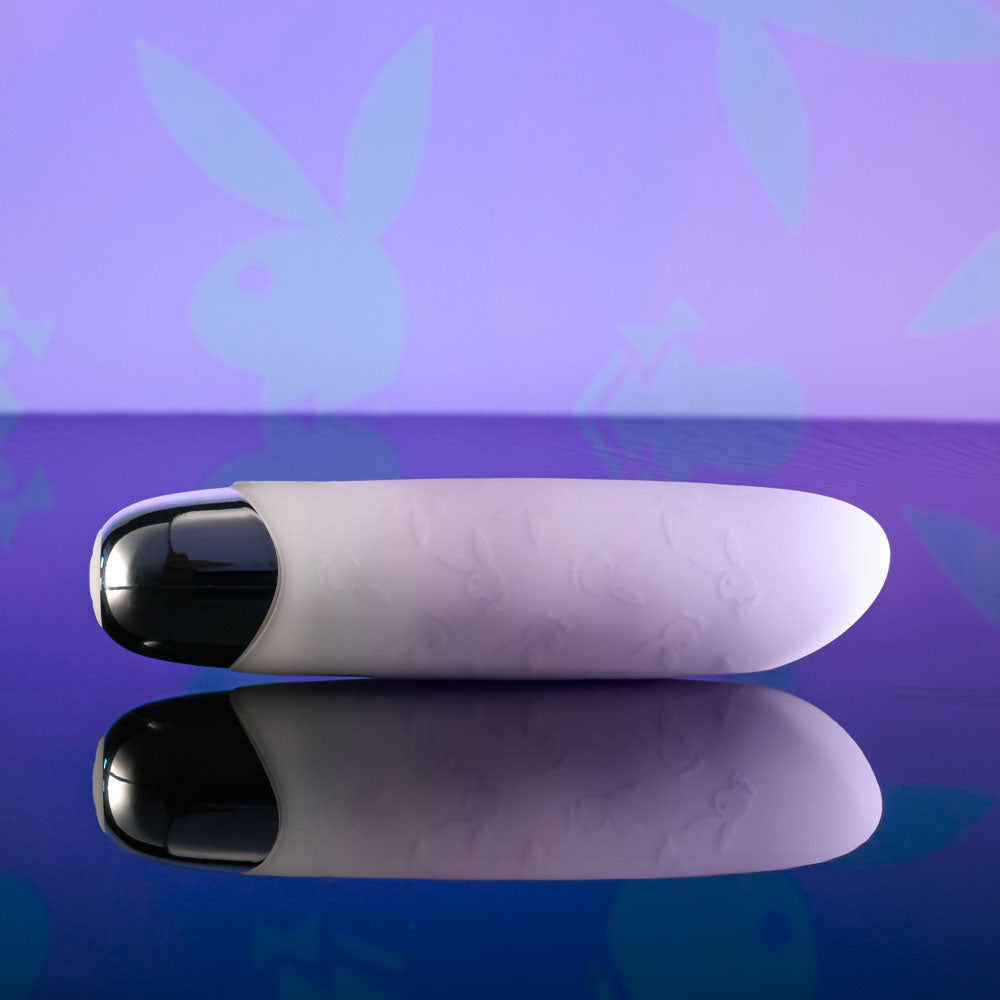 Playboy Pleasure BUNNY BUNCH - Pearl 11.3 cm USB Rechargeable Bullet on a reflective surface with a playful background.