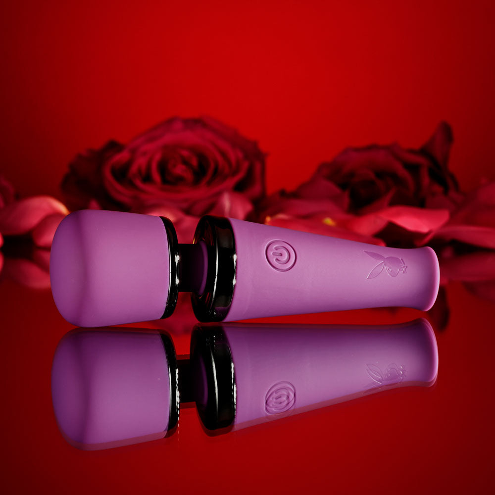 Playboy Pleasure MIC DROP - 11.4 cm USB Rechargeable Vibrating Mini Massage Wand on a reflective surface with roses.
