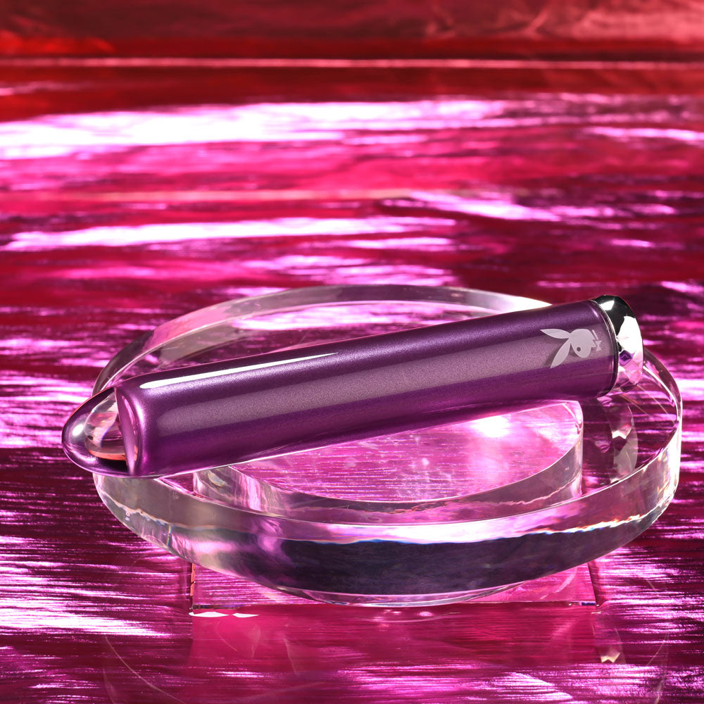 Playboy Pleasure AMETHYST - 12.4 cm USB Rechargeable Glass Tipped Mini Vibrator on a clear stand with pink background