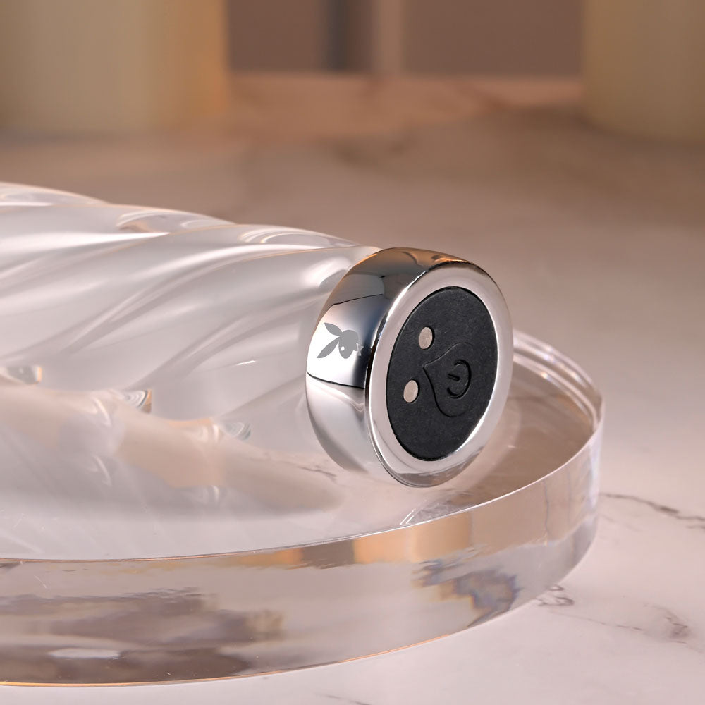 Playboy Pleasure IN A TWIST - Glass 17.5 cm USB Rechargeable Vibrator with spiral design and silver accents on a marble surface.