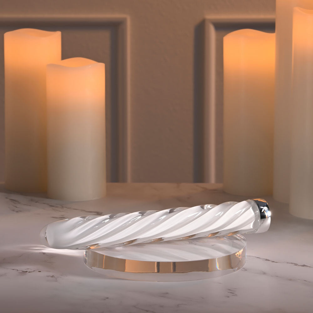 Playboy Pleasure IN A TWIST -  Glass 17.5 cm USB Rechargeable Vibrator displayed elegantly on a marble surface with candles.