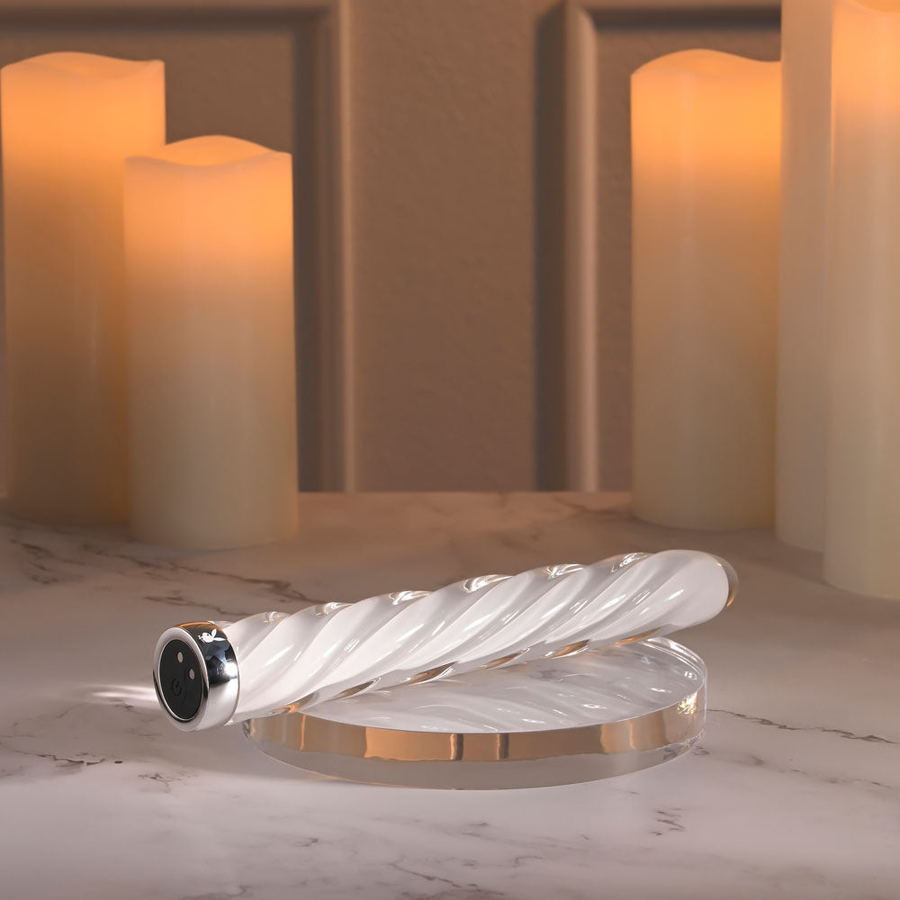 Playboy Pleasure IN A TWIST -  Glass 17.5 cm USB Rechargeable Vibrator on a marble surface with candles in the background.