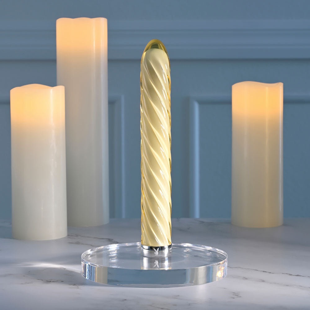Playboy Pleasure TWIST OF FATE USB rechargeable glass vibrator on a marble surface surrounded by soft glowing candles.