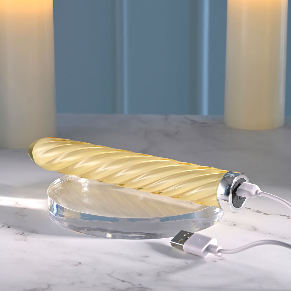 Playboy Pleasure TWIST OF FATE - Glass 17.5 cm USB Rechargeable Vibrator on a marble surface with charging cable.