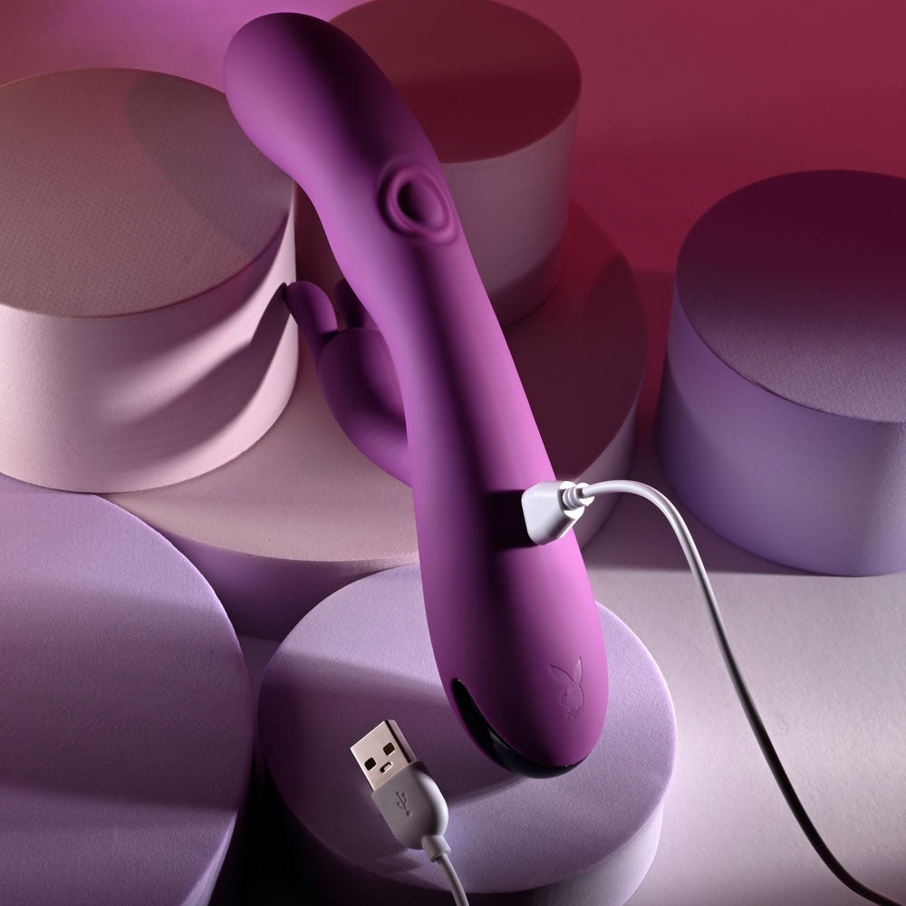 Playboy Pleasure BUSY BUNNY - 22.6 cm USB Rechargeable Rabbit Vibrator with Tapping Shaft charging on pastel background.
