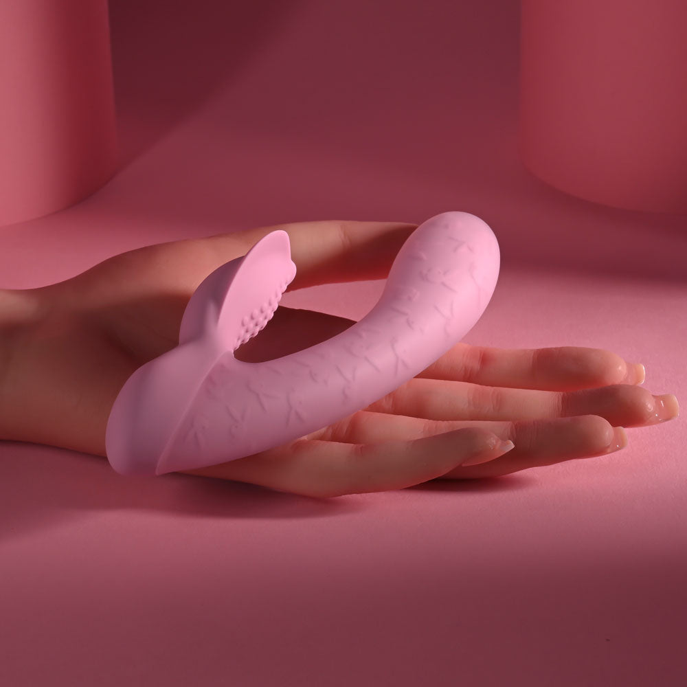 USB rechargeable rabbit vibrator in pink silicone, resting on a hand against a pink background.