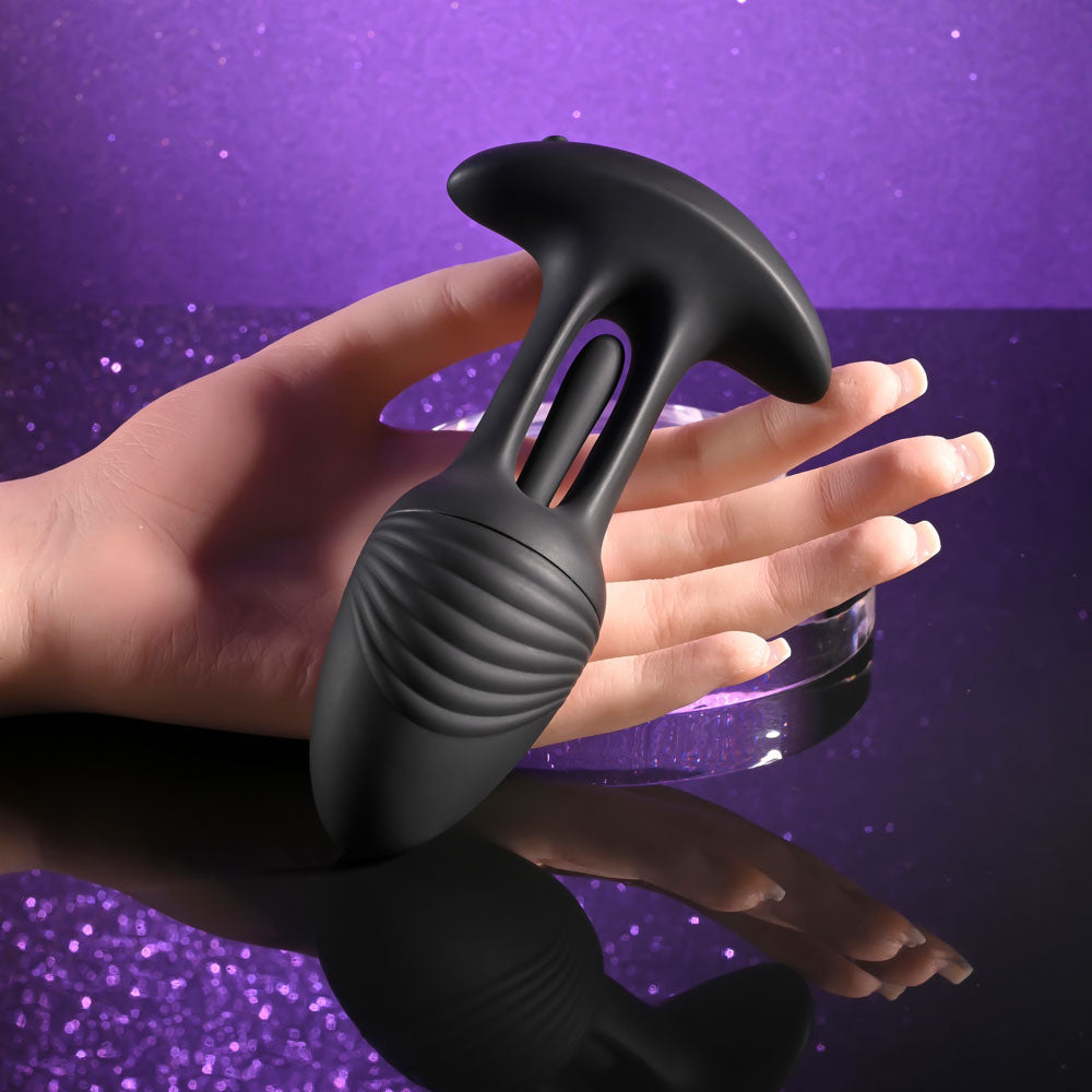 Playboy Pleasure RIM SHOT - 11.4 cm USB Rechargeable Vibrating Butt Plug on a hand with a purple glitter background.