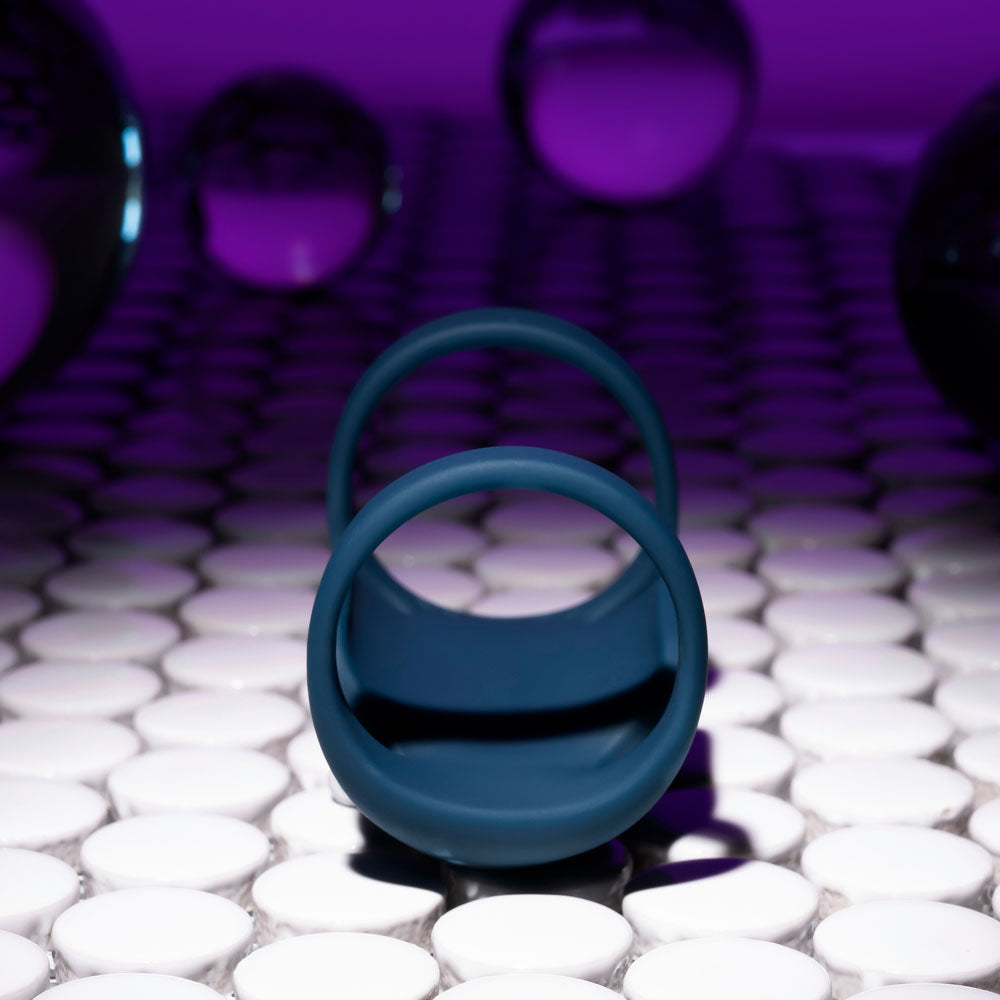 Playboy Pleasure JET PACK - Dark USB Rechargeable Vibrating Penis Harness on a background of glossy white and purple spheres.