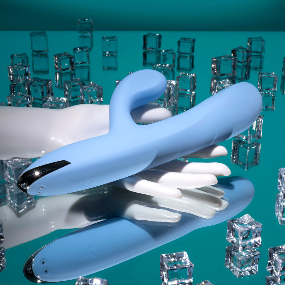 Playboy Pleasure UP AND AWAY - 26.7 cm USB Rechargeable Rabbit Vibrator resting on reflective surface with ice cubes.