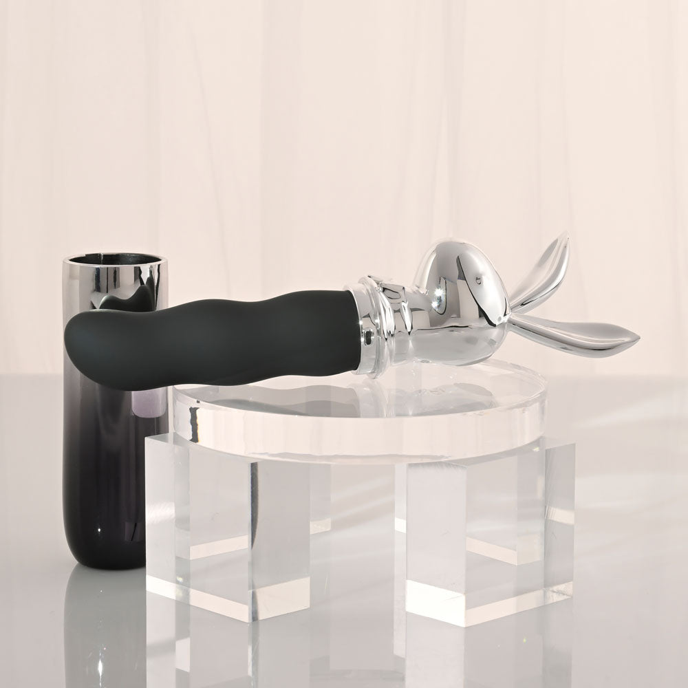 Playboy Pleasure BUNNY ON THE GO - /Chrome 18.6 cm USB-C Rechargeable Vibrator displayed on a clear pedestal.