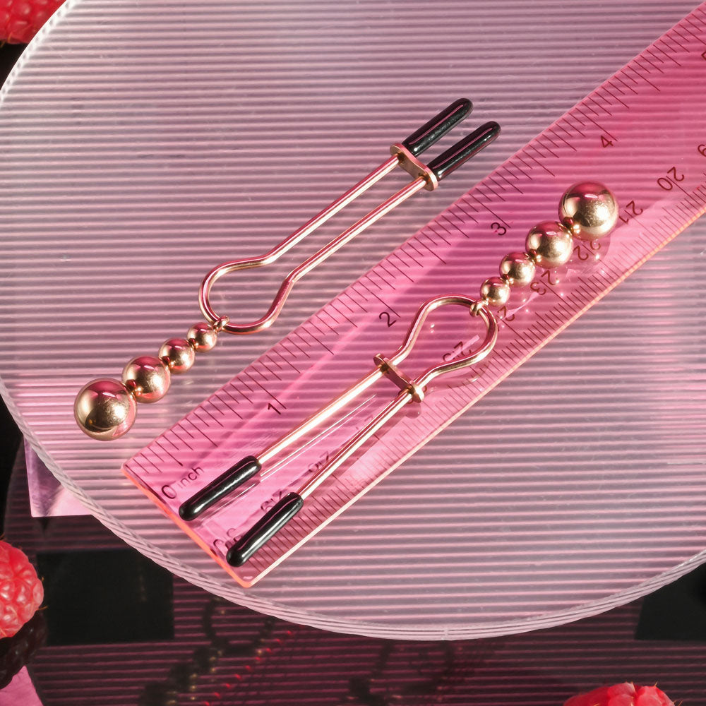 Selopa BEADED NIPPLE CLAMPS -  -  Nipple Clamps - Set of 2 on a ruler with pink background and decorative elements.