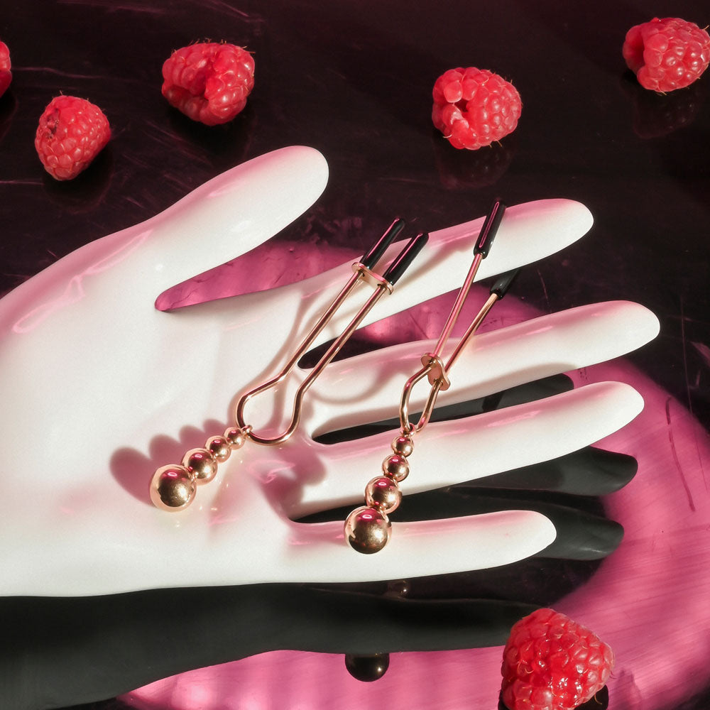Selopa BEADED NIPPLE CLAMPS -  -  Nipple Clamps - Set of 2 displayed on a hand surrounded by raspberries.