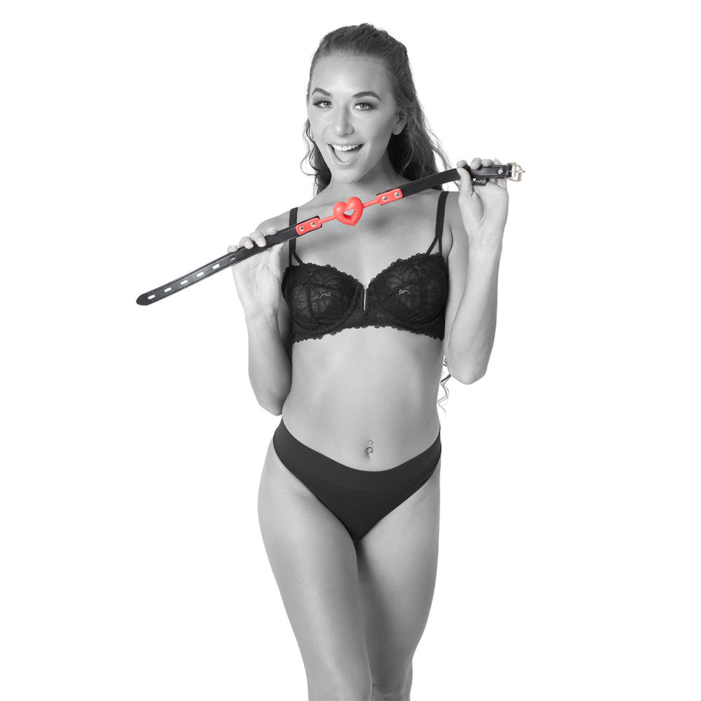 Sex & Mischief Amor Ball Gag - /Black Mouth Restraint held by a model in lingerie, showcasing its heart-shaped design.