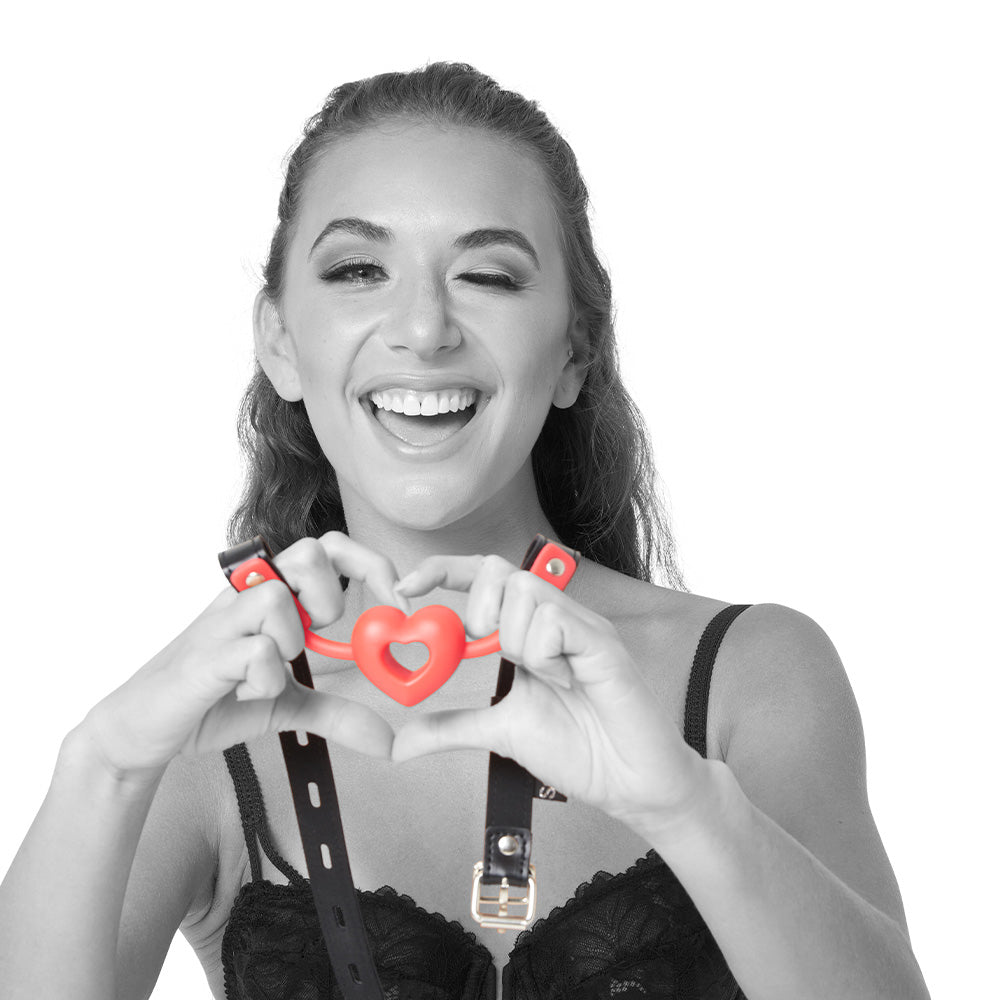 Sex & Mischief Amor Ball Gag - /Black Mouth Restraint model displaying heart gag with smile in intimate setting.