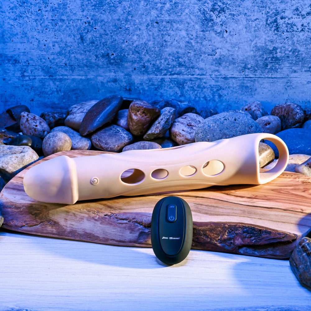 Zero Tolerance BIG BOY EXTENDER - Light -  USB Rechargeable Vibrating Penis Extension Sleeve beside remote on wood.